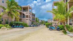 A resort with multiple-story buildings, palm trees, and golf carts parked on a gravel road. - Waterfront resort villa with water views, balcony, full kitchen, & washer dryer (San Pedro)