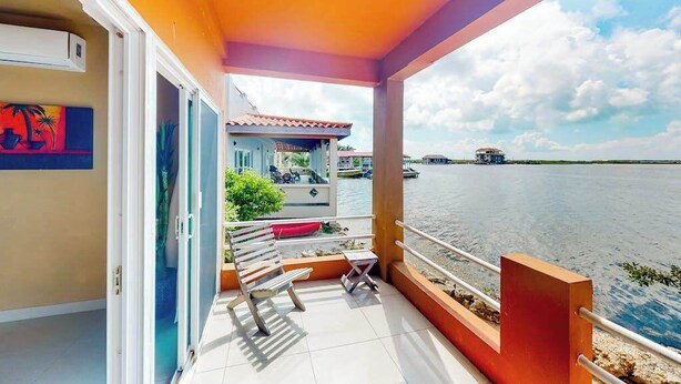 A balcony with a view of the water, a chair, a small table, and a door leading to a room. - Waterfront resort villa with water views, balcony, full kitchen, & washer dryer (San Pedro)