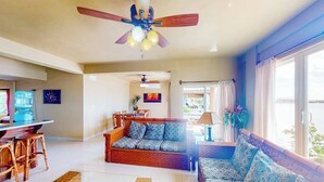 A spacious living area with a sofa, wooden chairs, a dining table, and a ceiling fan. - Waterfront resort villa with water views, balcony, full kitchen, & washer dryer (San Pedro)