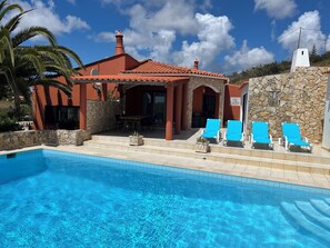 Un espace piscine doté d’une piscine à l’eau cristalline, de chaises longues et d’une terrasse avec une table et des chaises.