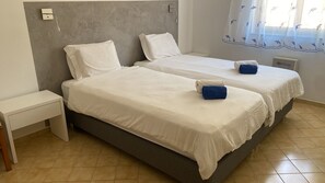 A double room with two beds, a nightstand, and a window with a curtain.