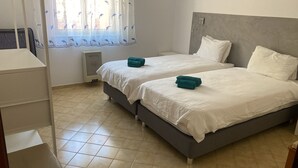 Hotellihuone, jossa on kaksi sänkyä, patteri, ikkuna, jossa on verho, ja yöpöytä.