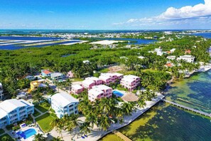 Vista aérea de un balneario costero con varios edificios, una piscina y un muelle que se adentra en el agua.