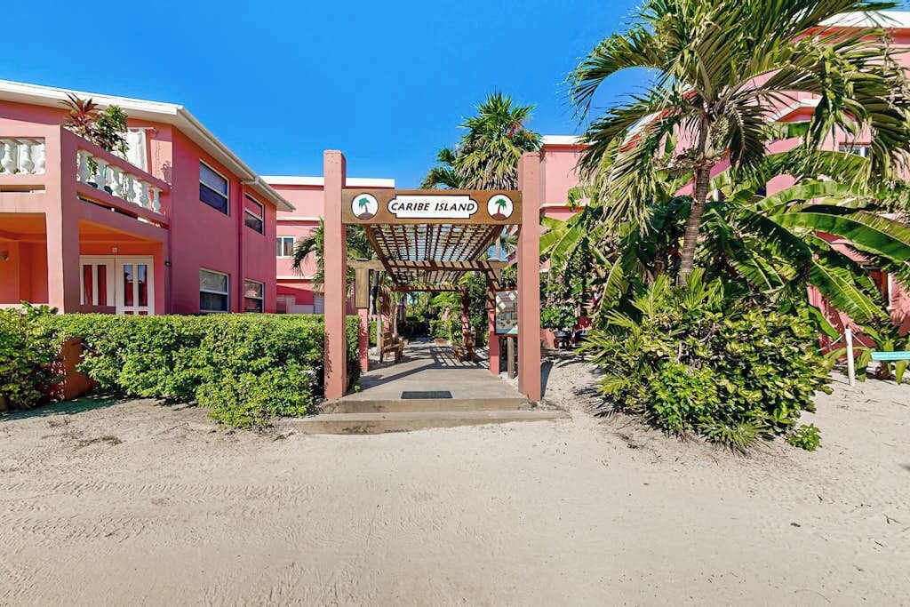 A hotel entrance with a sign reading 'Caribe Island,' surrounded by palm trees and a sandy path.