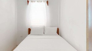 A single bed with white bedding, wooden headboard, and a window with a sheer curtain. - Enchanting single-level living space with a mini kitchen in a prime area (Caye Caulker)
