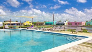 A swimming pool with lounge chairs, a wooden deck, and colorful buildings in the background. - Renovated 2BR with Sunset Views at Mara Laguna (San Pedro)