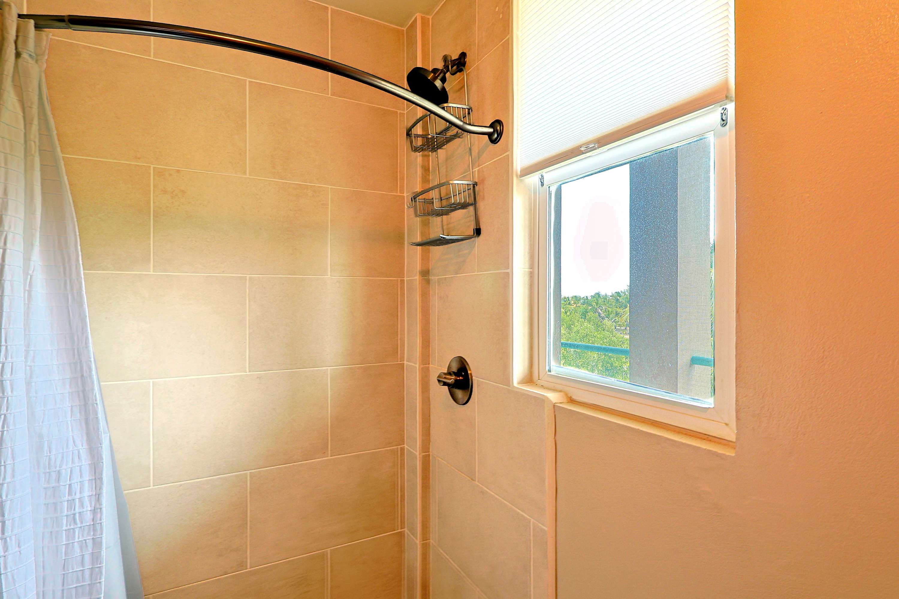 A shower area with a curved showerhead, a window with a view, and a towel rack.
