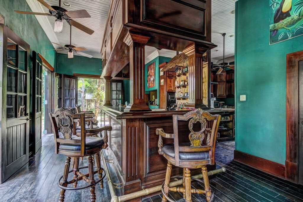Un espace bar avec des chaises en bois et un comptoir, des murs verts et un ventilateur de plafond.