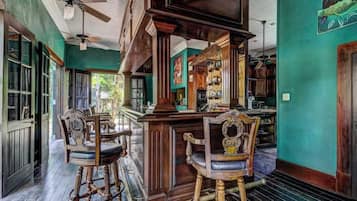 Un espace bar avec des chaises en bois et un comptoir, des murs verts et un ventilateur de plafond.