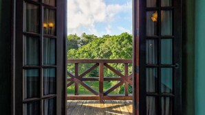 Eine offene Holztür führt zu einem Balkon mit Blick auf eine grüne Landschaft.