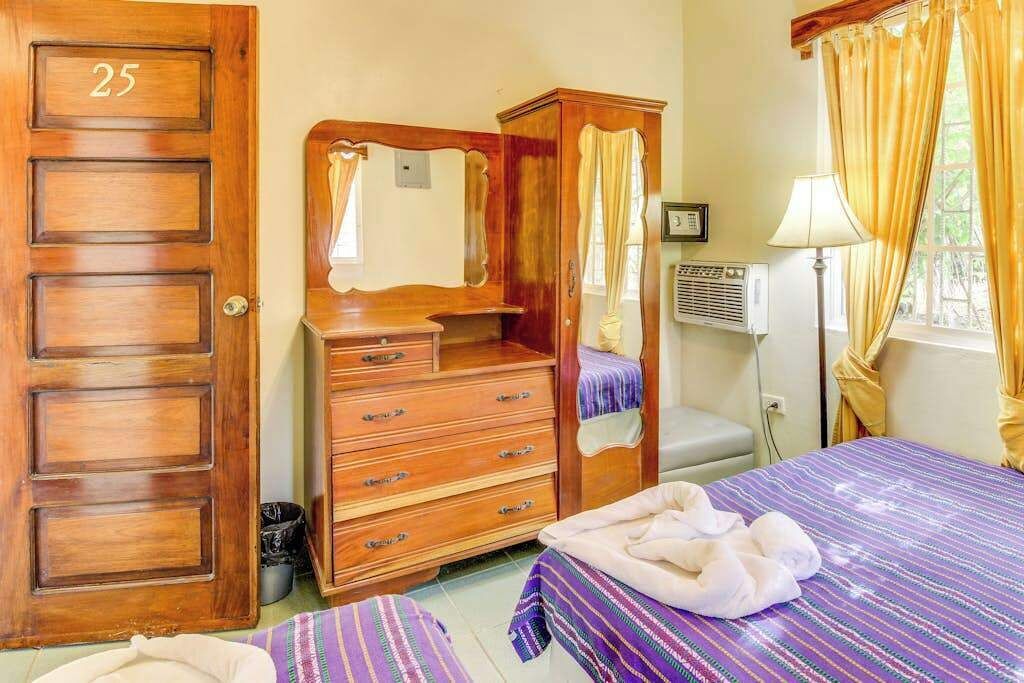 Ein Zimmer mit Holzschrank, Bett mit gestreifter Bettdecke, Fenster mit Vorhängen und Heizkörper.