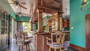 A bar area with wooden chairs, a bar counter, and a ceiling fan. - Riverfront Suite, Lovely View, Partial AC, WiFi & Pool (San Ignacio)