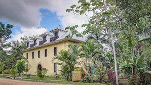 A two-story building with a yellow facade, a balcony on the upper floor, and a sign indicating it is a Mahogany Inn. - Riverfront Suite, Lovely View, Partial AC, WiFi & Pool (San Ignacio)