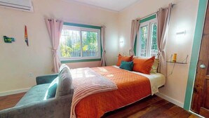 A bedroom with a bed, a window, a door, and a wall-mounted air conditioner. - Charming retreat with spacious outdoor areas, cozy interior & near to beach (Placencia)