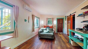 A room with a sofa, a table, and a kitchen area with shelves. - Charming retreat with spacious outdoor areas, cozy interior & near to beach (Placencia)