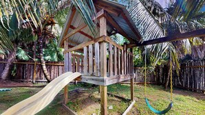 A wooden playhouse with a slide and a hanging swing. - Charming retreat with spacious outdoor areas, cozy interior & near to beach (Placencia)