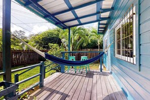 Varanda coberta com uma rede, deck de madeira e um edifício azul com janelas.