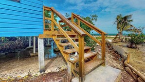 Una escala de fusta que condueix a un edifici blau, amb vistes al mar i palmeres.