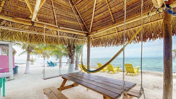Una cabana a la vora de la platja amb teulada de palla, seients de fusta i un hamaca.