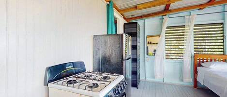 Une cuisine équipée d’une cuisinière à gaz, d’un four et d’un réfrigérateur, une table en bois et un lit avec du linge de lit blanc.