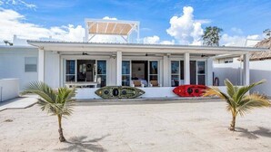 Een modern huis met een overdekt terras, een surfplank en palmbomen.