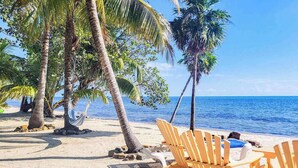 Een strand met palmbomen, een hangmat en houten stoelen.
