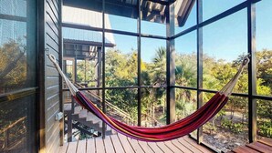 A hammock on a wooden deck with a view of a house and surrounding greenery.