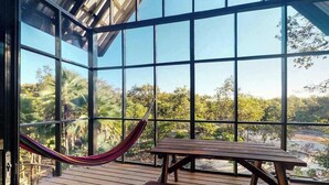A wooden deck with a hammock and a picnic table, large windows offering a view of greenery.