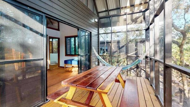 A wooden deck with a picnic table, large windows, and a hammock.