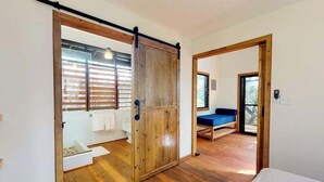 A room with a wooden floor, a sliding door, a bed, a bench, and a view through a window.