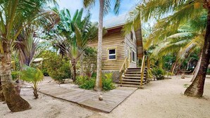 A wooden house with a wooden deck, surrounded by palm trees and tropical vegetation. - Romantic beachfront home w ocean views, dock, hammock, veranda & free WiFi (Placencia)