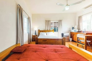 Une chambre à coucher comprenant un lit, un bureau, une chaise, un ventilateur de plafond et une fenêtre.