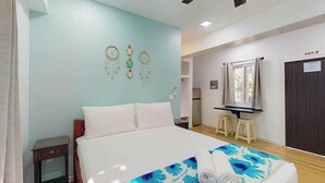 Una habitación de hotel con cama, mesita de noche, escritorio con taburetes, espejo y puerta con letrero de SALIDA.