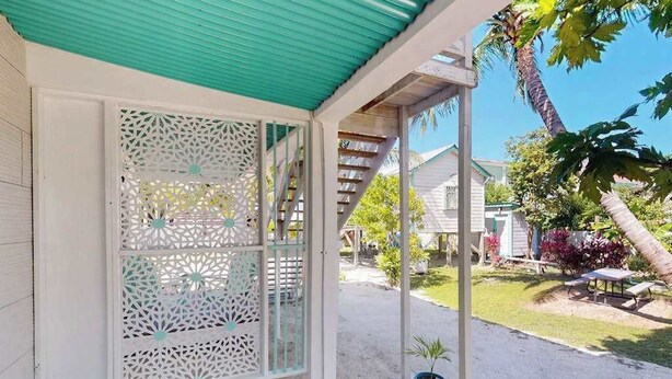 Un espacio al aire libre cubierto con una estructura blanca, una escalera de madera y un pequeño jardín con una palmera y una planta en maceta.