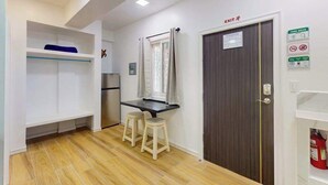 Cocina compacta con refrigerador, una mesa y taburetes, y una puerta con el rótulo 'EXIT'.