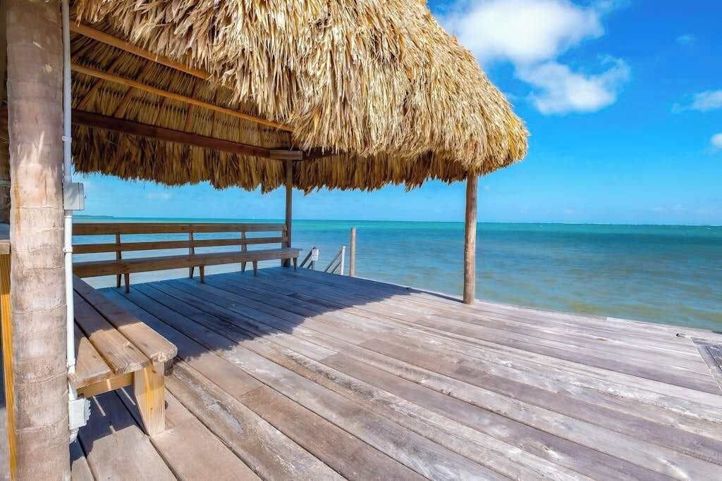 Une terrasse en bois surmontée d’un toit de chaume, offrant une vue sur une mer calme.