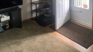 Ein Wohnzimmer mit Fernseher, Schuhregal, einer Tür mit Weihnachtskranz und Blick ins Freie.