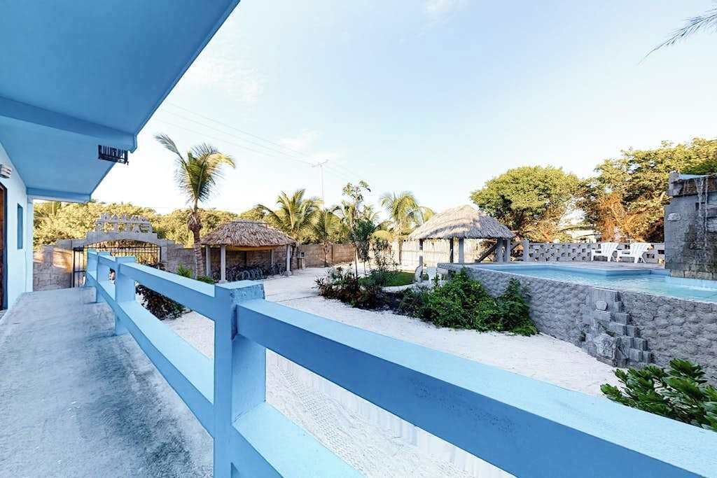 A pool area with a blue railing, thatched-roof structures, and palm trees.