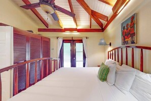 Een slaapkamer met een bed, houten balken in het plafond, een plafondventilator, een schilderij aan de muur en een raam met gordijnen.