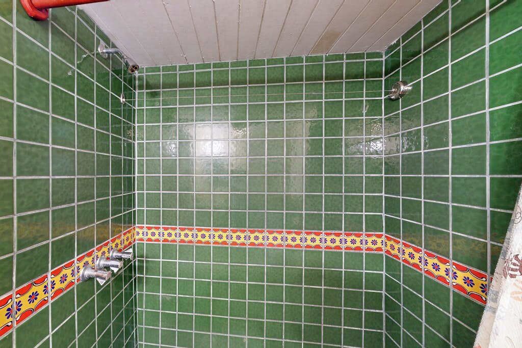 Un bagno con pareti rivestite di piastrelle verdi, una bordura decorata e un angolo doccia con un tubo rosso.