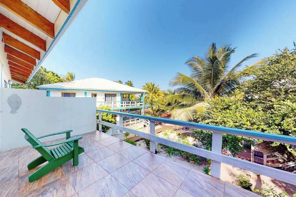 Un balcon avec une chaise verte, un bâtiment blanc en arrière-plan et une végétation luxuriante tout autour.
