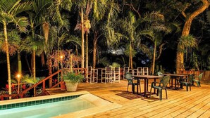 Um deck de madeira com piscina, cercado por palmeiras e um cercado de madeira.