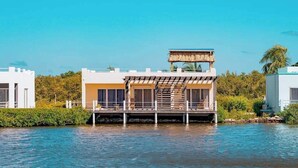 Une maison flottante dotée d’une terrasse, entourée d’eau, sous un ciel dégagé.