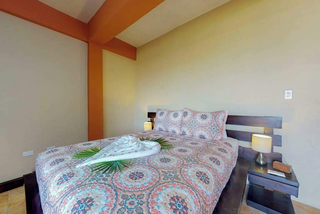 Un letto rifatto con una coperta a motivi, una lampada da comodino e un tavolino con una sveglia.