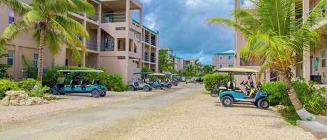 A resort with multiple-story buildings, palm trees, and golf carts parked on a gravel road.