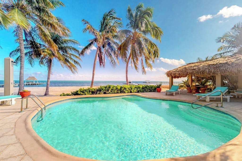 A pool with clear water, surrounded by palm trees and a beach view.