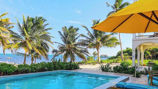 A pool with clear blue water, surrounded by palm trees and a view of the ocean. - Beachfront condo with pool, amazing ocean view, & W/D - near restaurants (San Pedro)