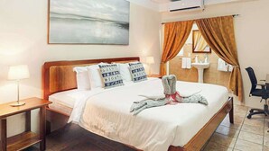 Habitación de hotel con una cama grande, una mesita de noche, un escritorio, una silla, una ventana con cortinas, un cuadro en la pared y un lavamanos.