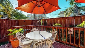 Una terraza de madera con una mesa redonda y sillas, un paraguas rojo y una planta en maceta.
