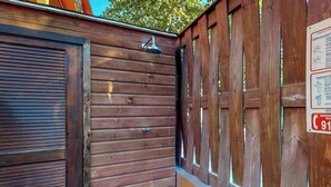 Una cerca de madera con un portón metálico, una puerta de madera y un cabezal de ducha metálico.